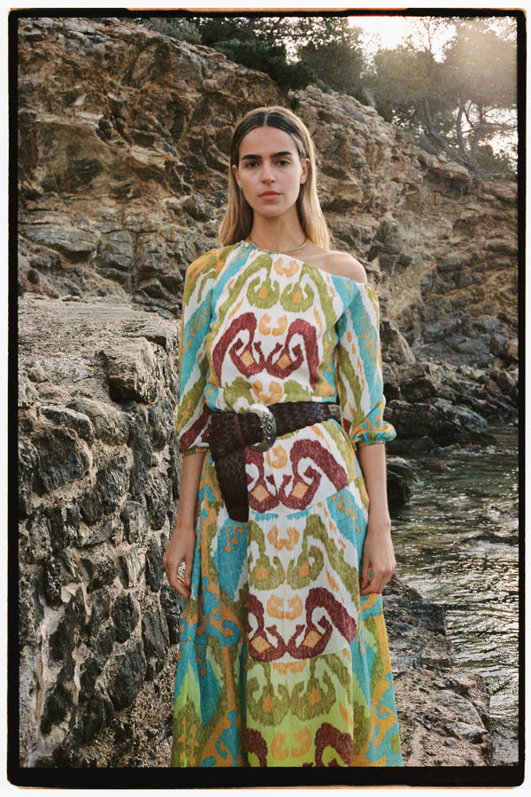Michonet – Robe Ikat Delhi, modella con abito lungo stampato colorato e cintura intrecciata, in posa davanti al mare