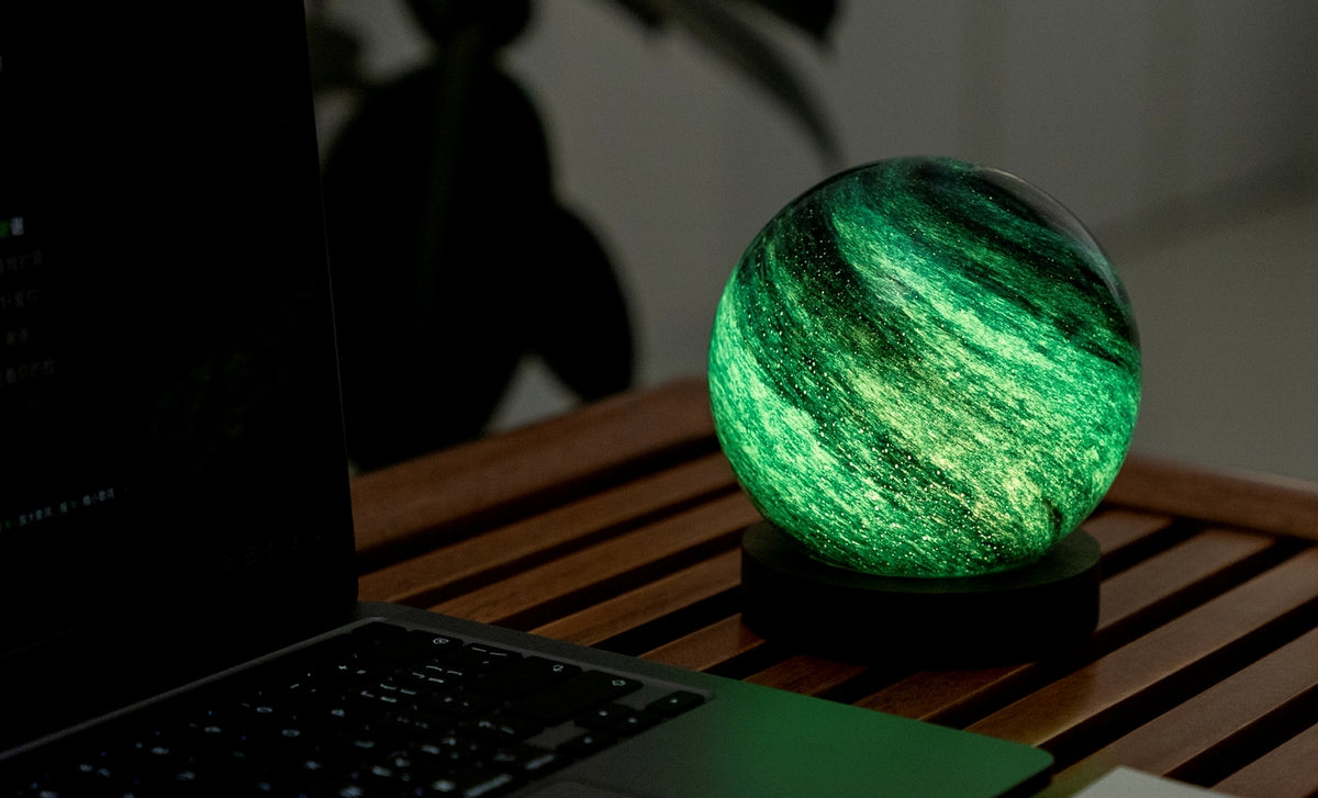 Gingko Design – Astraglass Leuchte - Stellar Ocean - 2 Größen, kugelförmige grüne Leuchtschreibtischlampe neben einem Laptop