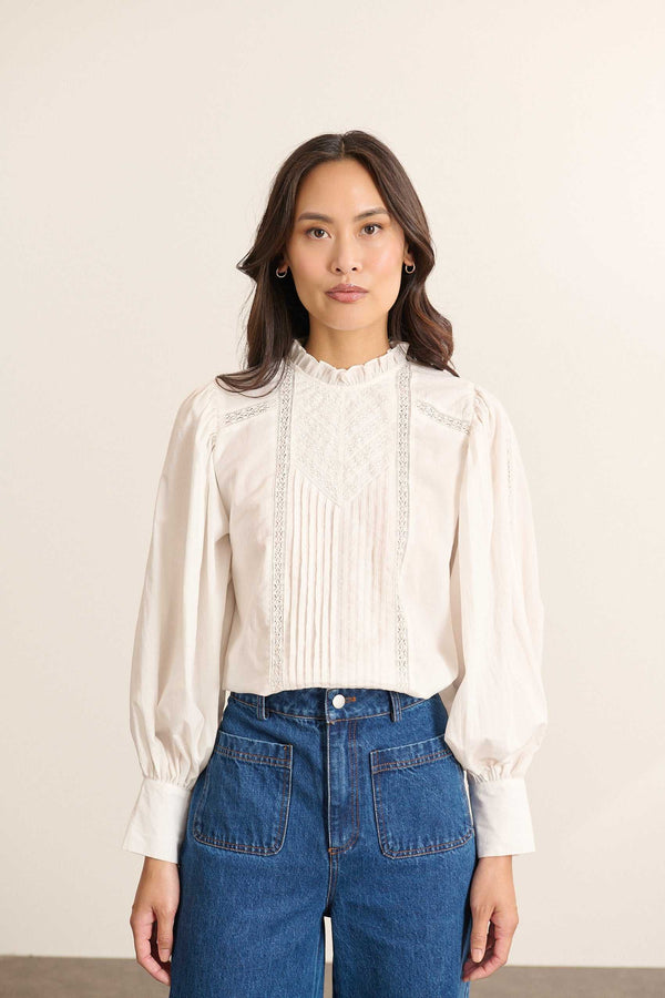 Modelo de frente con blusa holgada blanca de velo de algodón, cuello con volantes e inserciones de encaje.