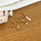 Instants Plaisirs – Set De Boucles D'Oreilles "Eclat" Acier, trois boucles d'oreilles dorées avec perles et pendentifs sur bois clair