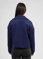 An'ge – Chaqueta Cassandra azul, mujer de espaldas con jersey azul marino de punto