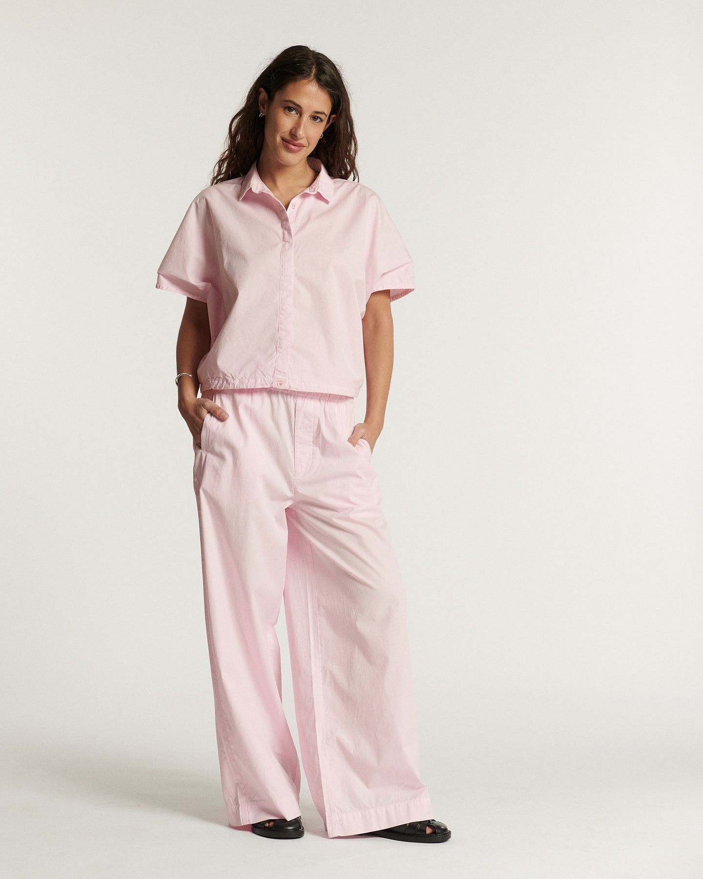 Light pink poplin pants, wide and fluid cut, light cotton material suitable for summer, offering comfort and an elegant silhouette.