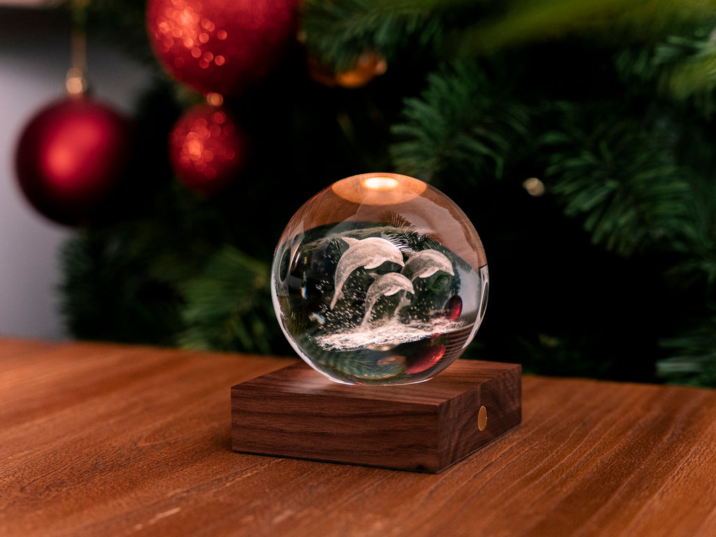 Gingko Design – Amber Crystal Leuchte - Delfine, eine leuchtende Glaskugel mit Delfinen auf einem Holztisch