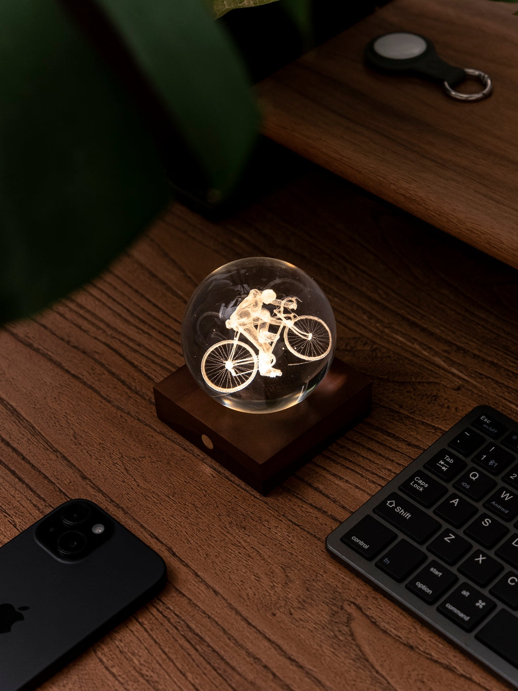 Gingko Design – Amber Crystal Light - Fietser, een oplichtende glazen bol met een fietser op een houten bureau