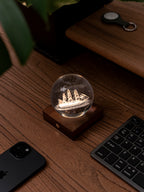 Gingko Design – Amber Crystal Leuchte - Segelboot, eine leuchtende Glaskugel mit einem Boot auf einem Holzschreibtisch