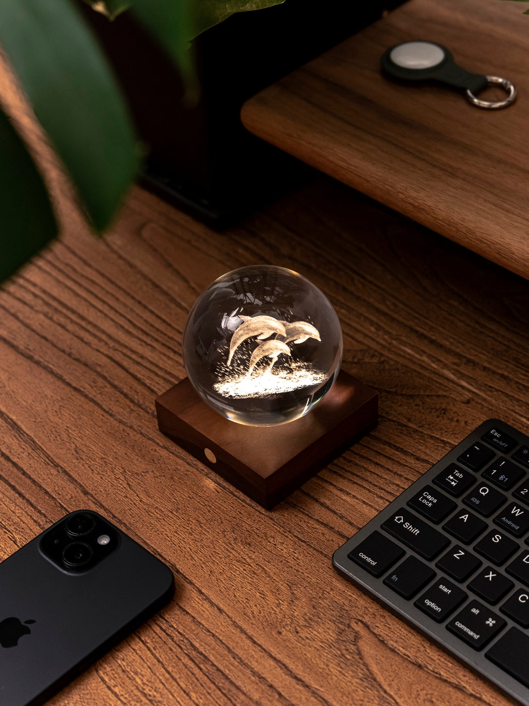 Gingko Design – Amber Crystal Leuchte - Delfine, eine leuchtende Kristallkugel mit Delfinen auf einem Holzschreibtisch