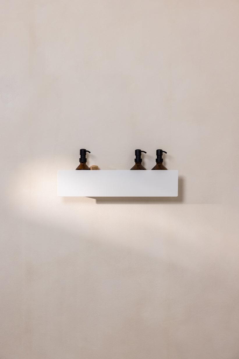 Duschablage SHEA in Weiß mit drei Flaschen für Duschzubehör an der Wand montiert.
