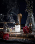 Sérum L'Élixir du Marabout de Garancia posé sur un vieux grimoire, entouré de fleurs rouges, de fioles d'apothicaire et d'une fumée mystique évoquant un laboratoire de sorcellerie.