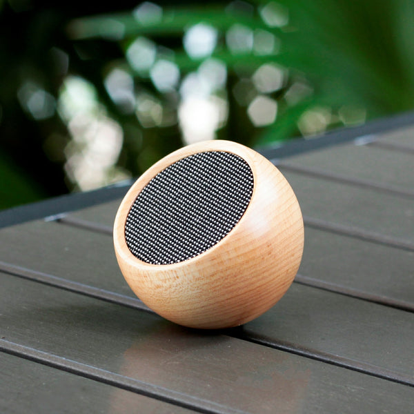 Gingko Design – Altavoz Tumbler Selfie - Arce Natural, altavoz Bluetooth de madera clara colocado sobre una mesa de madera