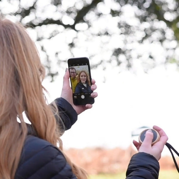 Gingko Design – Altavoz Tumbler Selfie - Arce Natural, una mujer rubia de espaldas se toma un selfie con un smartphone negro