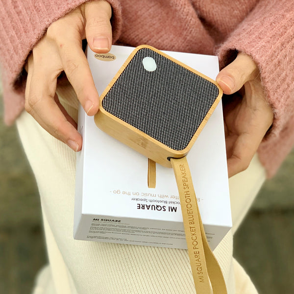 Gingko Design – Altavoz Bluetooth MI Square - Bambú Natural, una persona sostiene un altavoz portátil de madera y tela negra