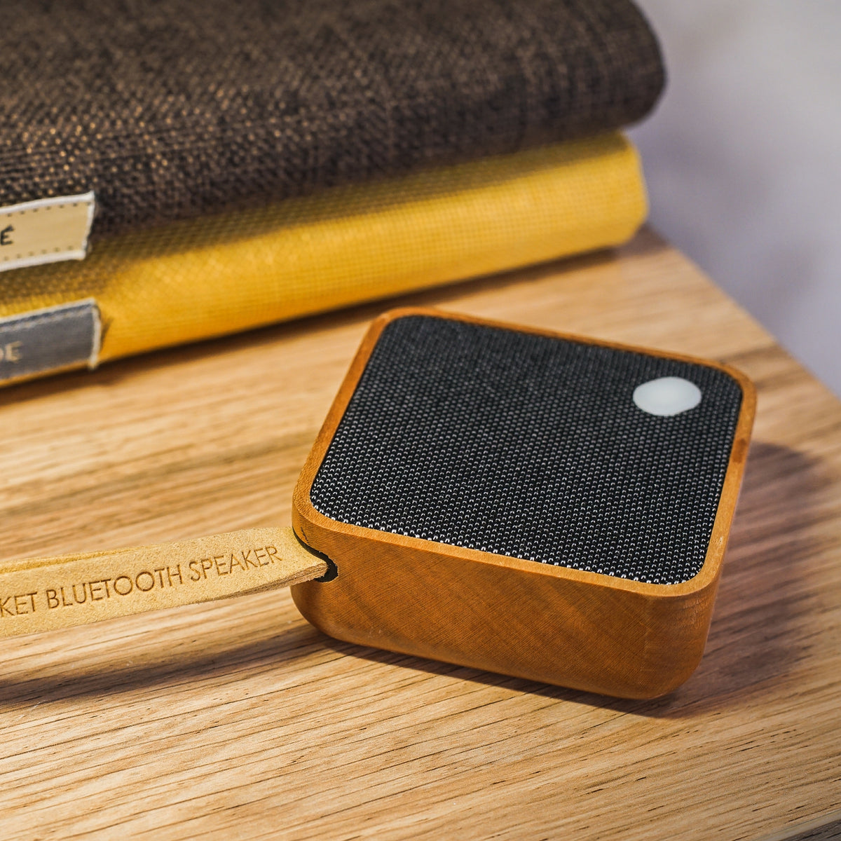 Gingko Design – Bluetooth-luidspreker MI Square - Natuurlijk kersenhout, bluetooth-luidspreker van licht hout en zwarte stof, op een houten tafel