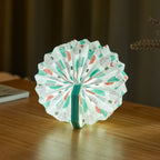 Gingko Design – Lampe Smart Accordion - Velours Bleu Géometrique, lampe éventail en papier blanc à motifs colorés, posée sur une table en bois