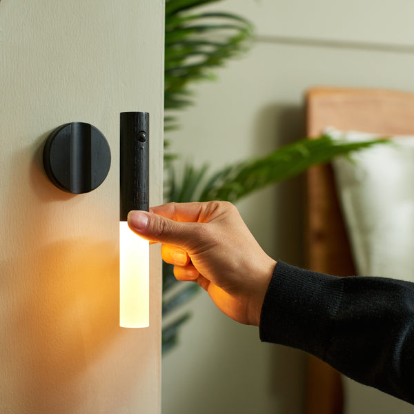 Gingko Design – Lampka Smart Baton - Heban, dłoń zdejmująca kinkiet z czarnego drewna dający ciepłe światło
