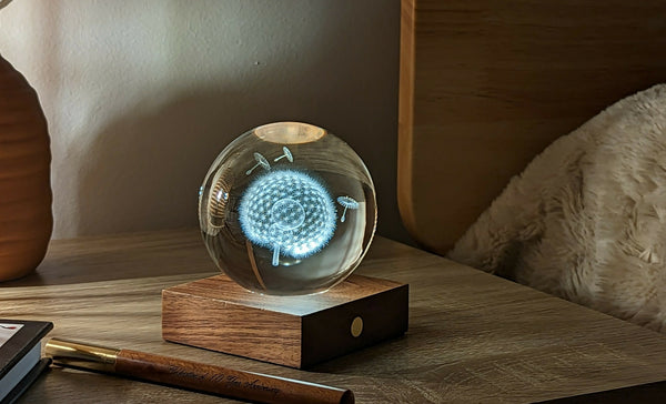 Gingko Design – Luz Amber Crystal - Diente de León, una bola de cristal luminosa con motivo de diente de león sobre una mesita de noche