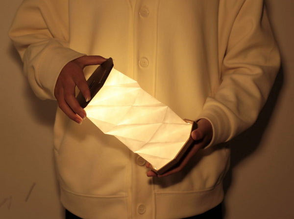 Gingko Design – Lampa Twist Hexagon - Lity Orzech, osoba trzymająca składaną lampę ze świecącego białego papieru