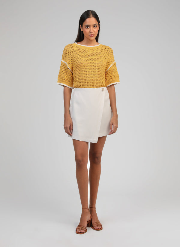 An'ge – Giovani Short Skirt Ecru, model wearing a yellow knitted jumper and a white skirt
