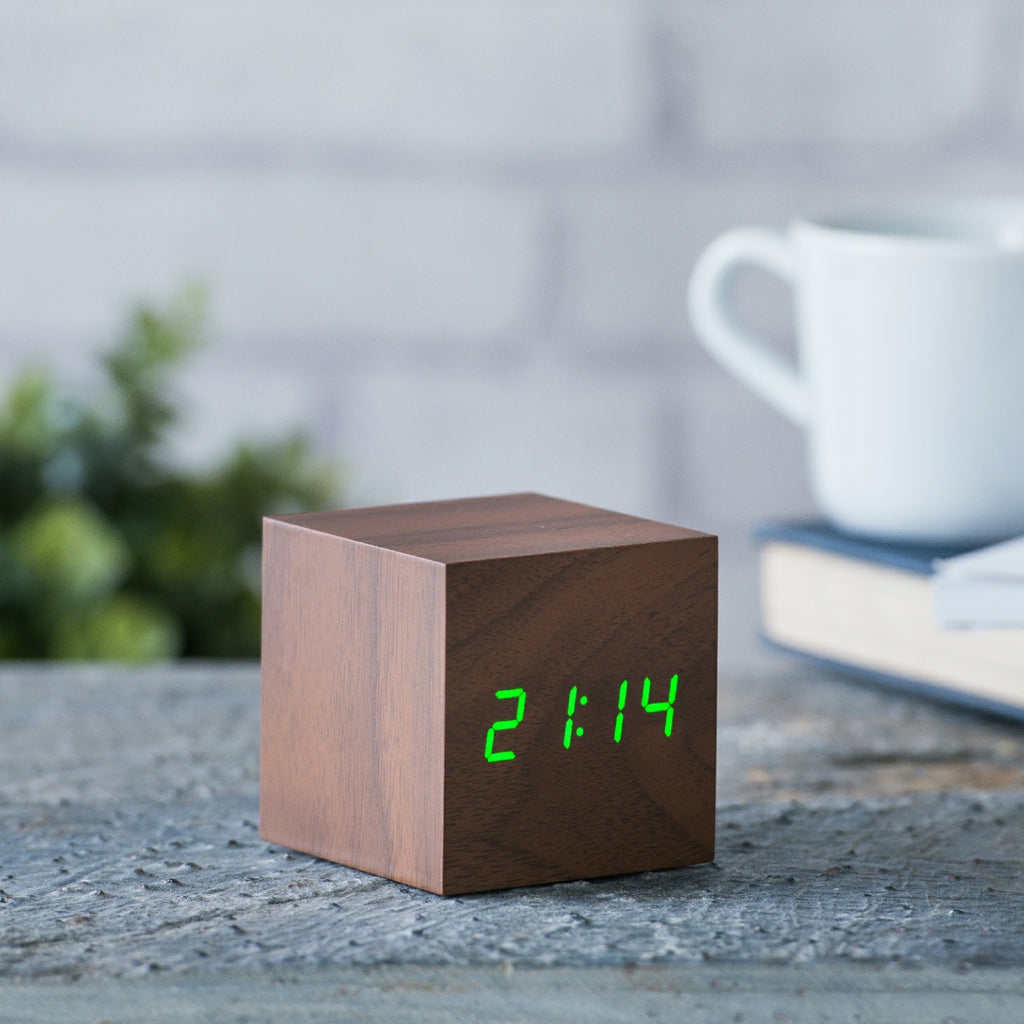 Gingko Design – Sveglia Wooden Cube Click - Noce / LED Verde, sveglia digitale in legno marrone, con orario visualizzato in verde, su un tavolo
