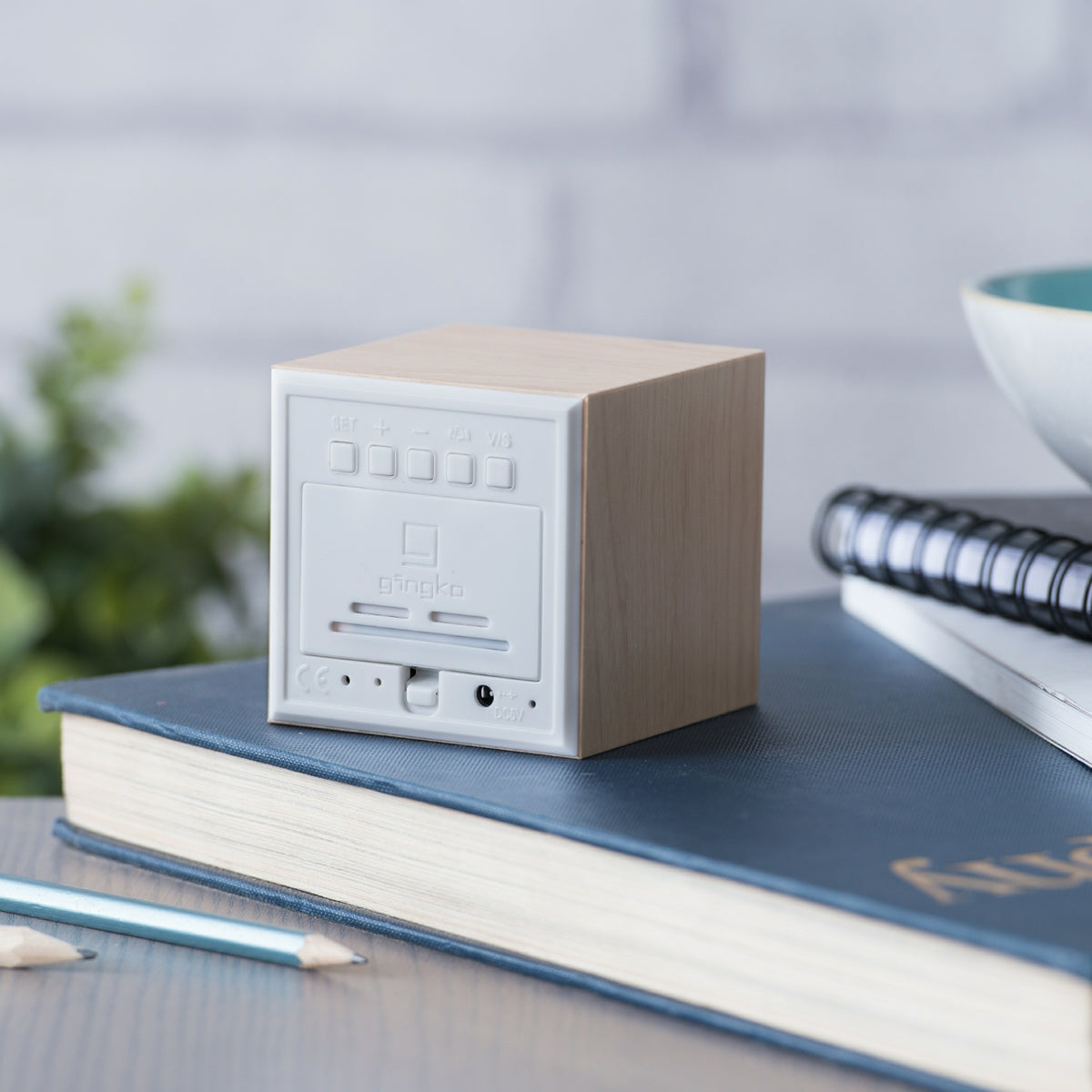 Gingko Design – Budzik Wooden Cube Click – Klon / Pomarańczowy LED, mały budzik z jasnego drewna stojący na ciemnoniebieskiej książce
