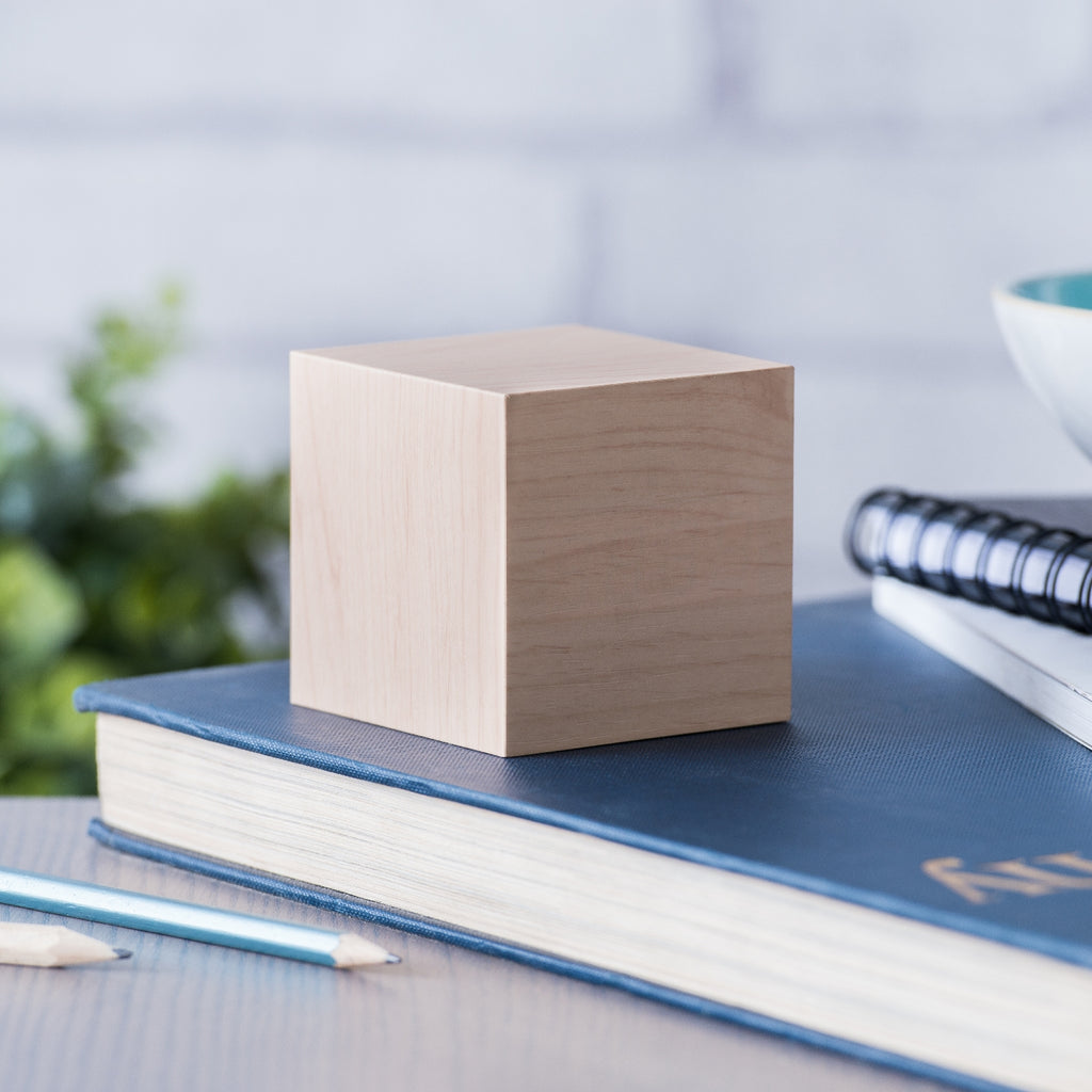 Gingko Design – Budzik Wooden Cube Click – Klon / Pomarańczowy LED, sześcian z jasnego drewna stojący na niebieskiej książce, z ołówkami