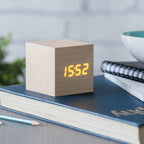 Gingko Design – Budzik Wooden Cube Click – Klon / Pomarańczowy LED, budzik w kształcie sześcianu z jasnego drewna wyświetlający godzinę na niebieskiej książce