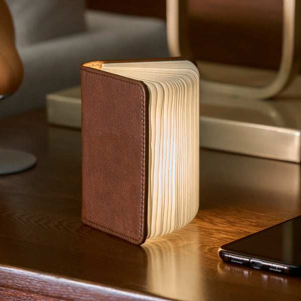 Gingko Design – Gingko Design - Lámpara Smart Book LED - Cuero Marrón - 2 Tamaños, lámpara con forma de libro abierto, colocada sobre una mesa de madera