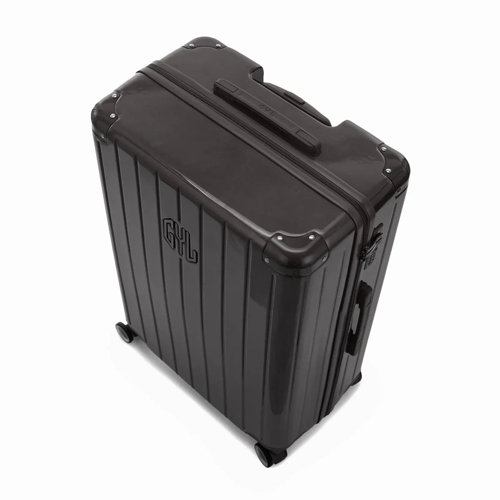 Angled view of the GYL Intemporelle black hard-shell suitcase with reinforced corners and glossy ribbed shell. #couleur_noir