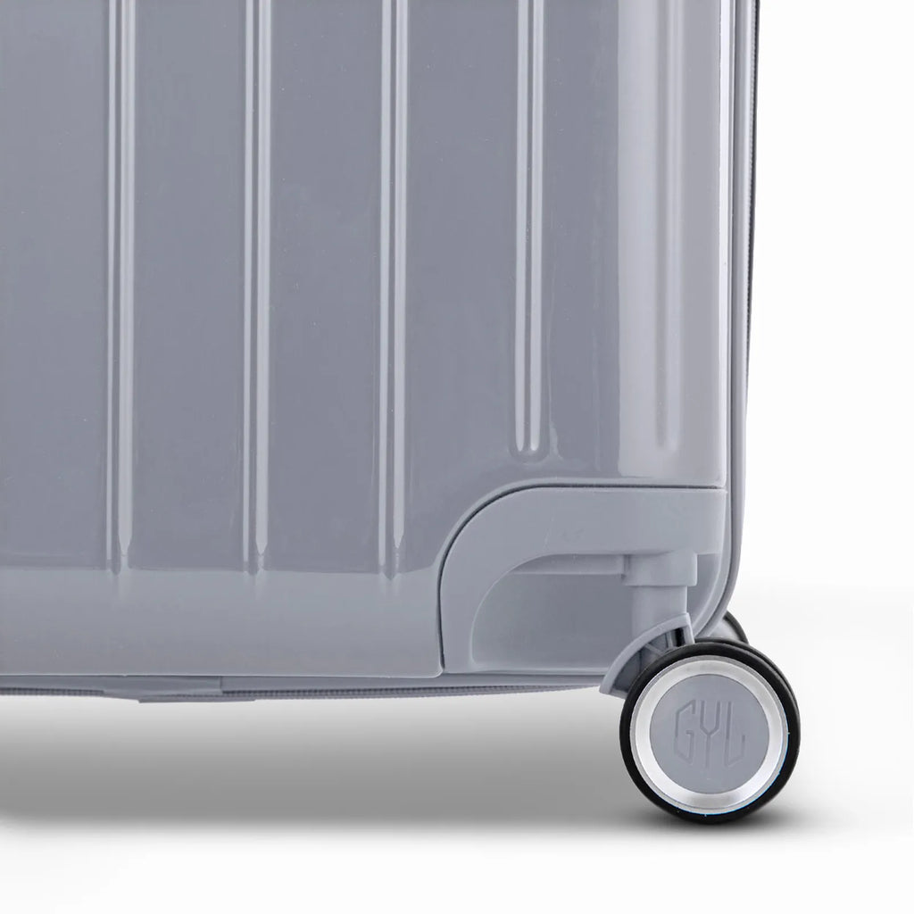 Detail of the wheel and GYL logo on the bottom of the silver trunk suitcase in glossy polycarbonate. #couleur_argent