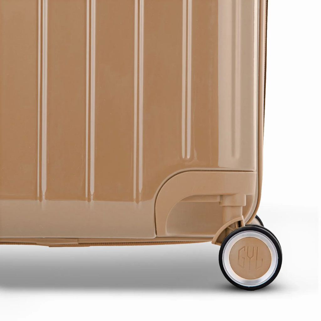 Detail of the wheel and GYL logo on the bottom of the champagne trunk suitcase in glossy polycarbonate. #couleur_champagne