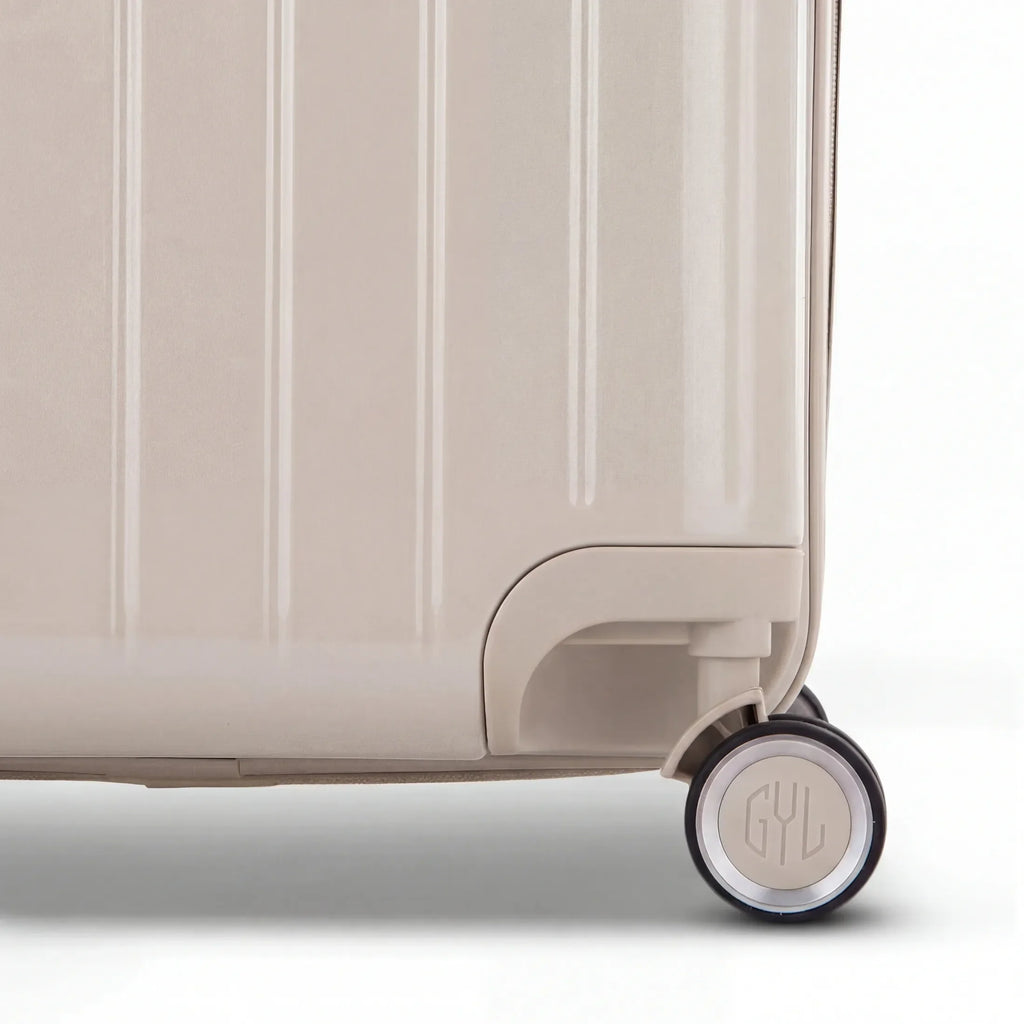 Detail of the wheel and GYL logo on the bottom of the nude trunk suitcase in glossy polycarbonate. #couleur_nude
