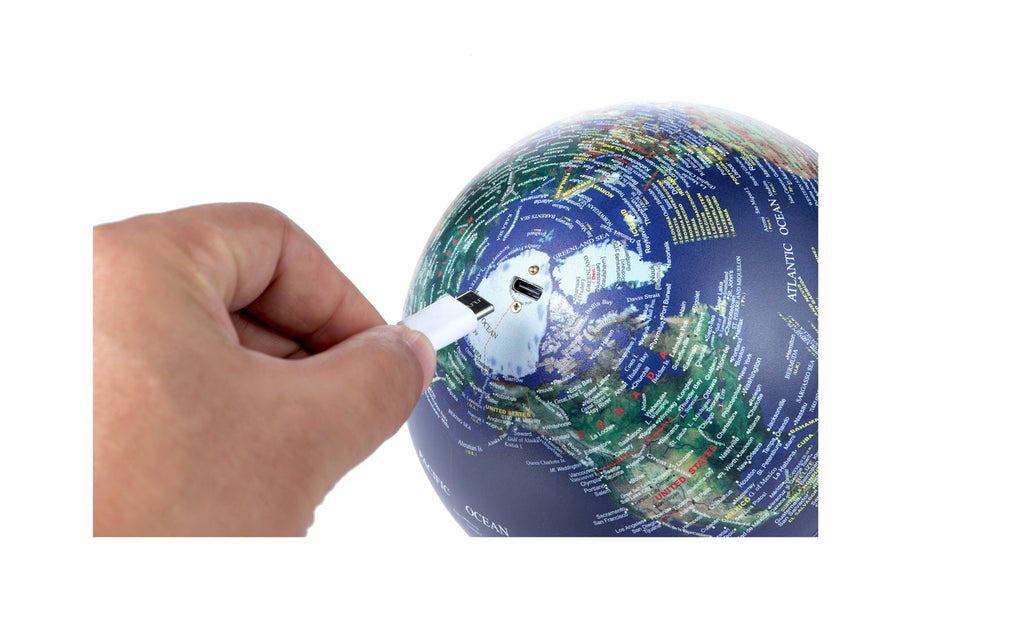 Gingko Design – Lampe Globe Atlas - Bleu Foncé / Socle Noyer - Mini, une main insère une clé USB dans un globe terrestre, sur fond blanc