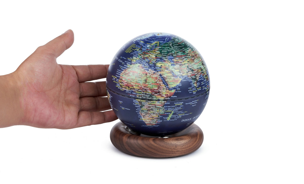 Gingko Design – Lampe Globe Atlas - Bleu Foncé / Socle Noyer - Mini, main tenant un globe terrestre bleu sur un socle en bois