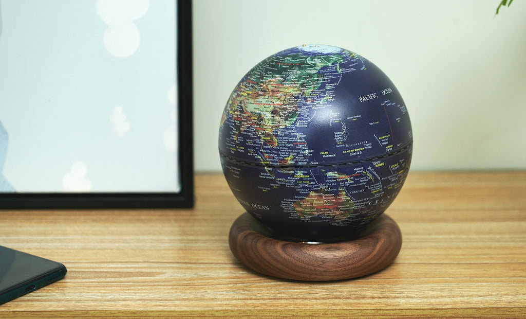 Gingko Design – Lampe Globe Atlas - Bleu Foncé / Socle Noyer - Mini, un globe terrestre bleu posé sur un socle en bois, sur un bureau