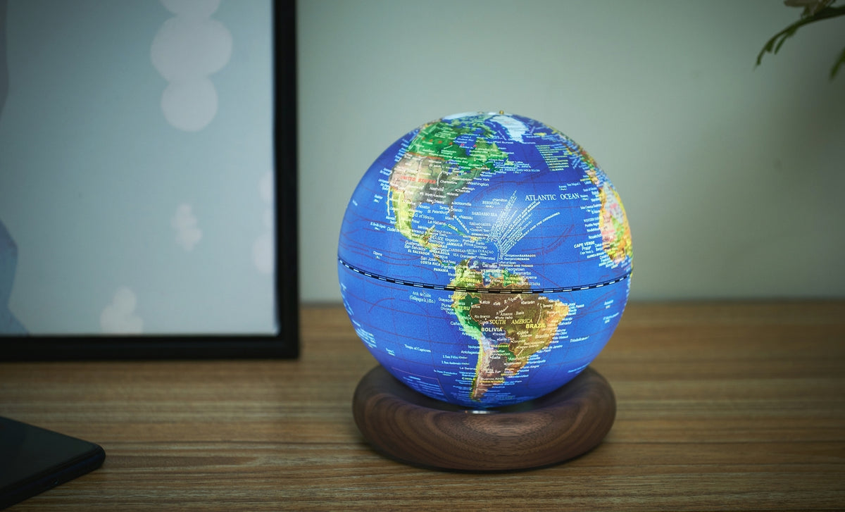 Gingko Design – Lampe Globe Atlas - Bleu Foncé / Socle Noyer - Mini, un globe terrestre lumineux posé sur un socle en bois