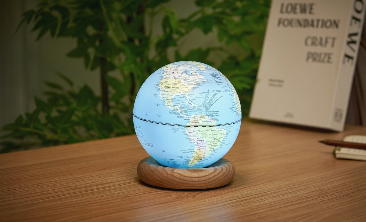Gingko Design – Lampada Mappamondo Atlas - Blu Chiaro / Base Frassino Bianco - Mini, mappamondo luminoso posato su una base in legno, su una scrivania