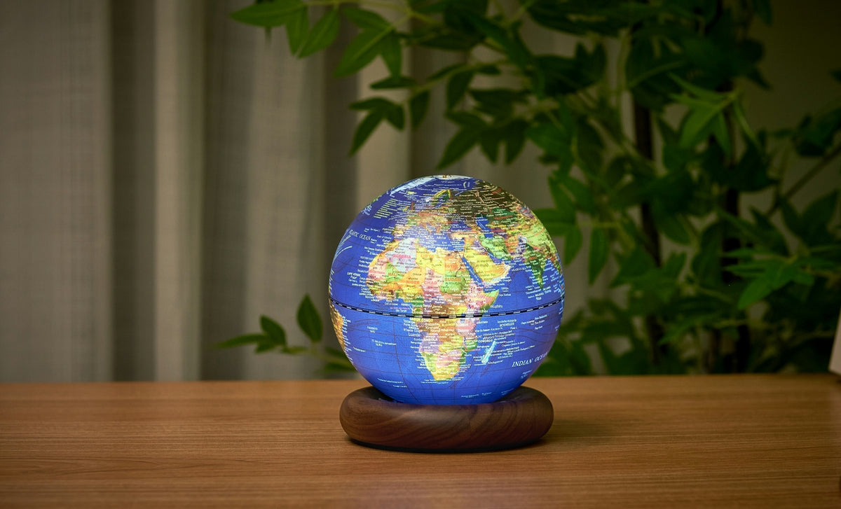 Gingko Design – Lampe Globe Atlas - Bleu Foncé / Socle Noyer - Mini, un globe terrestre lumineux posé sur un socle en bois, sur une table