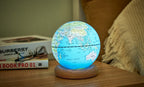 Gingko Design – Lampada Mappamondo Atlas - Blu Chiaro / Base Frassino Bianco - Mini, mappamondo luminoso posato su un comodino in legno