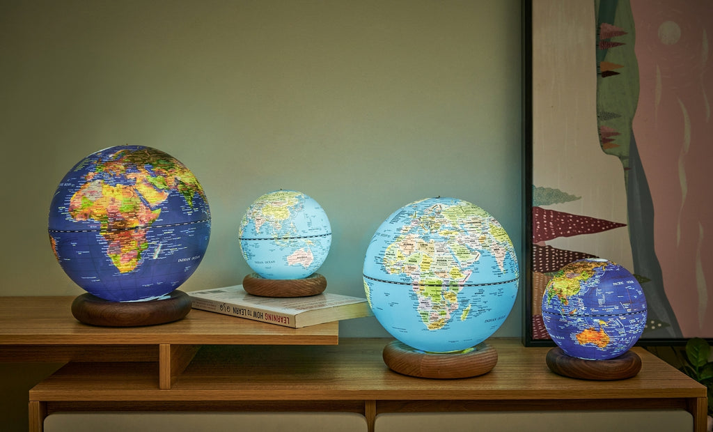 Gingko Design – Lampe Globe Atlas - Bleu Foncé / Socle Noyer - Mini, quatre globes terrestres lumineux de différentes tailles posés sur un meuble en bois