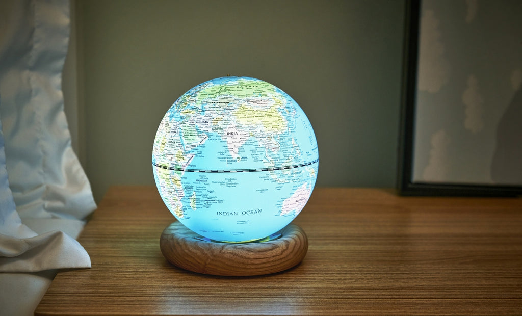 Gingko Design – Lampada Mappamondo Atlas - Blu Chiaro / Base Frassino Bianco - Mini, mappamondo luminoso posato su un comodino in legno