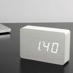 Gingko Design – Despertador Brick Click - Blanco / LED Blanco, despertador digital de madera clara que muestra la hora sobre una mesa oscura