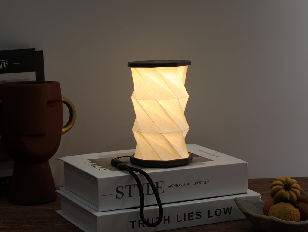Gingko Design – Lumière Twist Hexagon - Noyer Flotté - Mini, lampe de table pliable allumée, posée sur des livres, ambiance chaleureuse