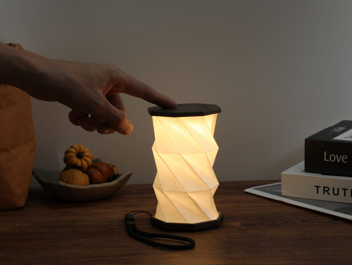 Gingko Design – Lumière Twist Hexagon - Noyer Flotté - Mini, lampe de table pliable allumée, main l'allumant, ambiance chaleureuse
