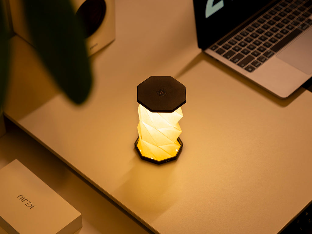 Gingko Design – Luz Twist Hexagon - Negro Pizarra - Mini, lámpara de mesa encendida sobre un escritorio con un ordenador portátil