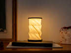 Gingko Design – Lumière Twist Hexagon - Noyer Flotté - Mini, lampe de table pliante en papier blanc allumée sur une table en bois