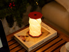 Gingko Design – Lumière Twist Hexagon - Rouge Corail - Mini, lampe de table rouge et blanche sur un livre