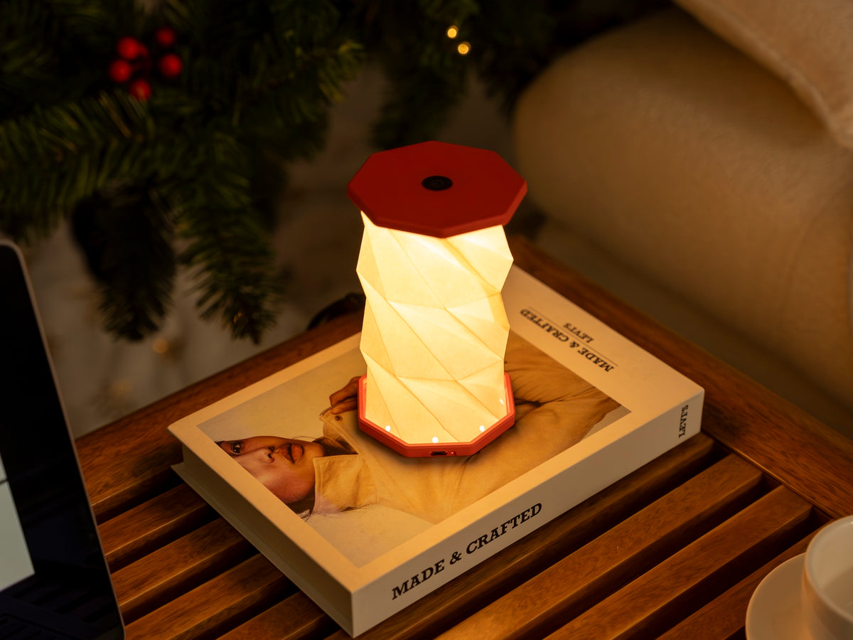 Gingko Design – Lumière Twist Hexagon - Rouge Corail - Mini, lampe de table rouge et blanche sur un livre