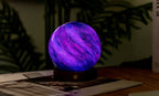 Gingko Design – Astraglass-lys - Galaxy Breeze - 2 Størrelser, kugleformet lilla og blå sengelampe på en træfod