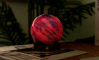 Gingko Design – Astraglass-lys - Galaxy Breeze - 2 Størrelser, kugleformet rød og lilla sengelampe på et træbord