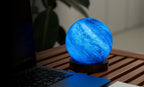 Gingko Design – Astraglass-lys - Galaxy Breeze - 2 Størrelser, blå sengelampe formet som en planet på et træbord