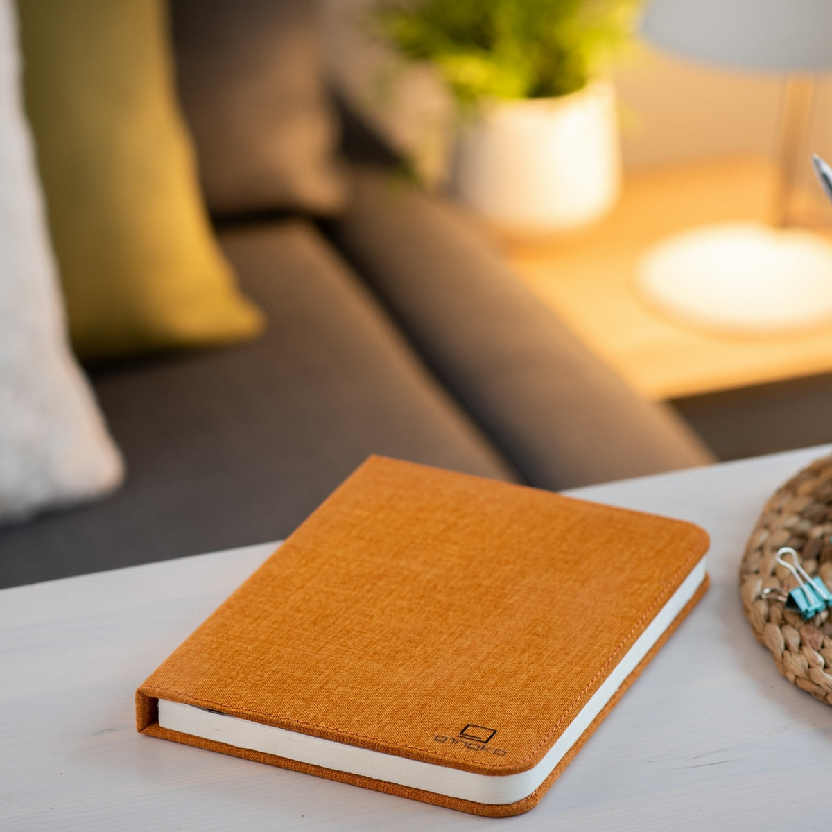 Gingko Design – Smart Book LED-lampe - Harmony Orange Hør - 2 Størrelser, orange notesbog på et sofabord i en stue